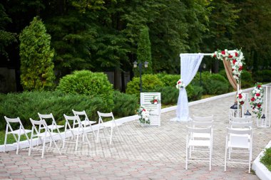 Güzel açık hava düğün süsleri, kırmızı ve beyaz çiçeklerle süslenmiş kemer, sandalyeler, fenerler..