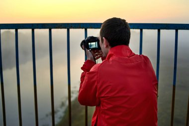 Nehrin üzerindeki bir köprüde sisli bir sabahta güneşin doğuşunu fotoğraflayan bir adam..