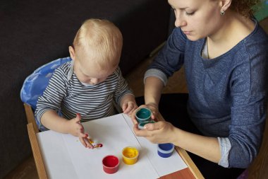 Anne, bir çocuğa parmak boyalarıyla resim yapmayı öğretir..