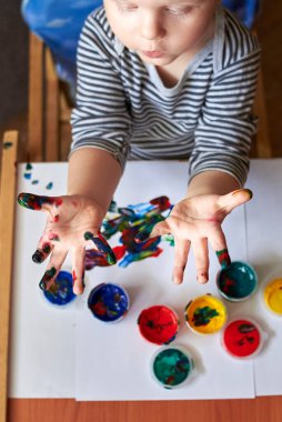 Çocuk, parmak boyalarıyla resim yaptıktan sonra kirli ellerini gösteriyor. Çocuğun ilk gelişimi..