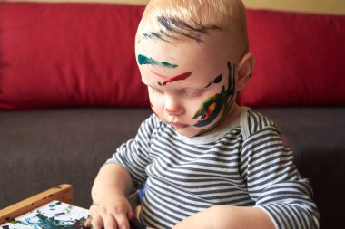 İyi lekelenmiş küçük bir çocuğun portresi. Parmak boyalarıyla çiziyor. Çocuğun erken gelişimi..