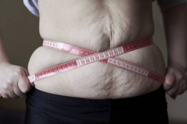 Kilo verme, diyet ve stres konuları olan şişkin bir göbeğin etrafına bir metre sarılmış bir kadın..