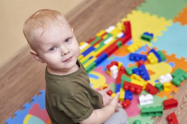 İki yaşında bir çocuk, bir evin zemininde renkli bir inşaatçıyla oynuyor. Çocuklar için eğitici oyunlar.