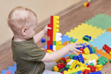 İki yaşında bir çocuk, bir evin zemininde renkli bir inşaatçıyla oynuyor. Çocuklar için eğitici oyunlar.