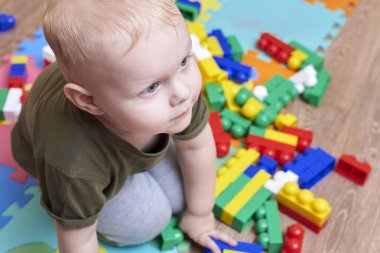 İki yaşında bir çocuk, bir evin zemininde renkli bir inşaatçıyla oynuyor. Çocuklar için eğitici oyunlar.