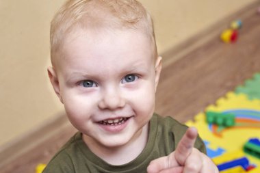 Oyuncakların arka planında gülümseyen mutlu bir çocuğun portresi, mavi gözlü, sarışın çocuk..