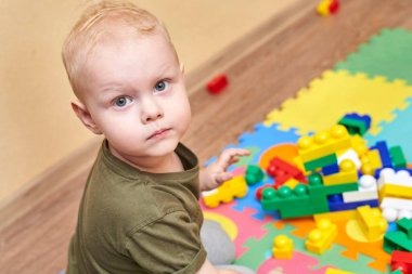 İki yaşında bir çocuk, bir evin zemininde renkli bir inşaatçıyla oynuyor. Çocuklar için eğitici oyunlar.