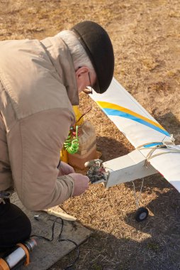 Bir adam, baharın başında sahada uçmak için uzaktan kumandalı bir uçak hazırlıyor..