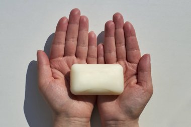 Beyaz arka plandaki bir kadının ellerinde beyaz bir sabun parçası, dezenfeksiyon teması ve enfeksiyonların yayılması ile mücadele.