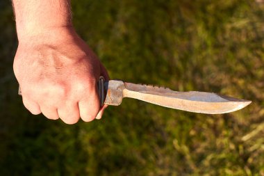 Arka planda adamın elinde keskin bir çentikli bıçak var..