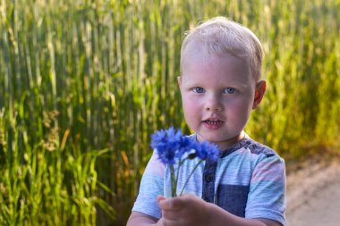 Küçük sarı saçlı çocuk elinde bir buket çiçek tutuyor, yaz temalı..