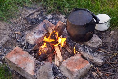 Bardağı olan eski bir çaydanlık doğada ateşte duruyor, kamp gezisinde çay hazırlıyor..