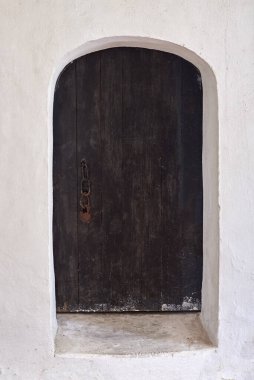 Beyaz bir duvarda paslı kilidi olan eski ahşap bir kapı, antik binalar..