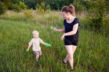 İki yaşındaki bir çocuk çayırda su tabancasıyla annesiyle oynuyor, yaz eğlencesi..