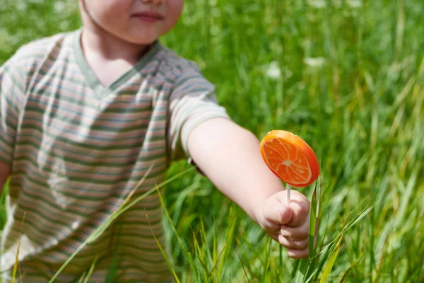 草を背景にカットオレンジの形でロリポップと小さな男の子の手 — ストック写真