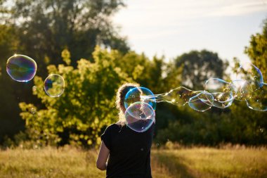 Yazın çayırda sabun köpüğü üfleyen bir kadın, yaz eğlencesi, yaz zamanı.