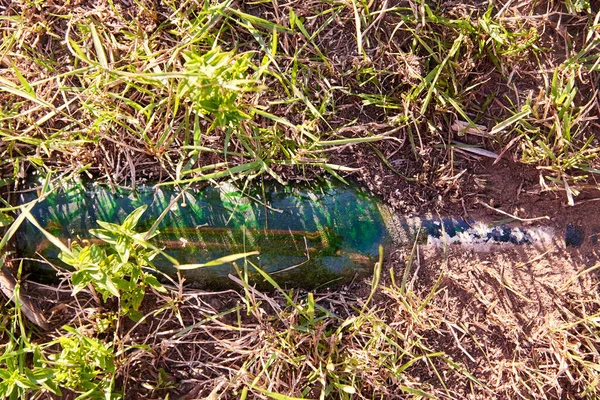 Glass bottle thrown out in nature and buried in the ground, environmental pollution, ecological problems.