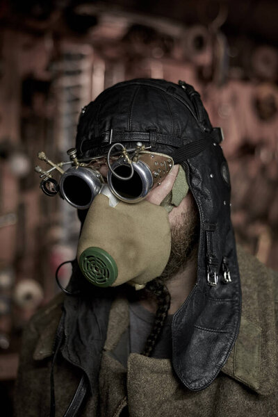 A bearded man in a respirator and glasses in the style of steampunk, dressed in an overcoat, postapokalipsis concept.