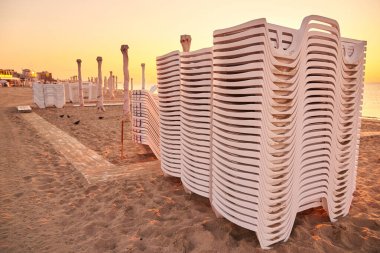 Gün doğumunda deniz sahilinde katlanmış güneş şezlongları ve şemsiyeler yeni bir güne hazırlanıyor..