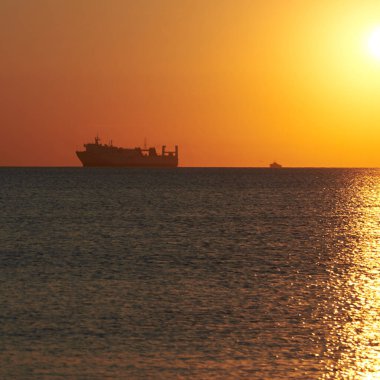 Denizde bulutsuz bir gökyüzünde gün batımı, ufukta bekleyen gemiler....