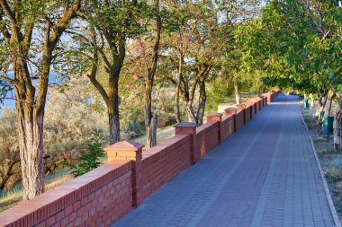 Şehir parkında boş bir sokak, banklar, çöp kutuları, tuğla bir çit..