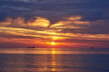 Denizde bulutsuz bir gökyüzünde gün batımı, ufukta bekleyen gemiler....