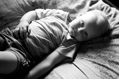 Küçük bir çocuk kanepede uzanıyor, gülümsüyor ve kameraya bakıyor, siyah beyaz bir fotoğraf..