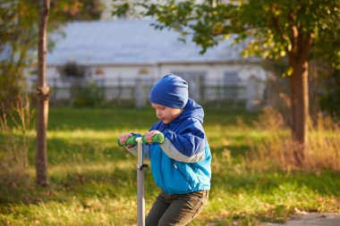 İki yaşında bir çocuk sonbaharda parkta scooter kullanıyor..