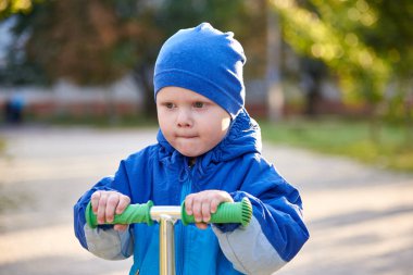 İki yaşında bir çocuk sonbaharda parkta scooter kullanıyor..