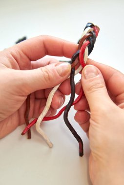 Kadının elleri beyaz arka planda deri bir bilezik yapıyor, yakın plan..