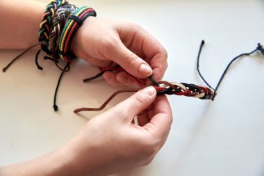 Kadının elleri beyaz arka planda deri bir bilezik yapıyor, yakın plan..