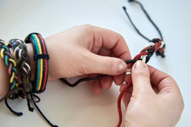 Kadının elleri beyaz arka planda deri bir bilezik yapıyor, yakın plan..