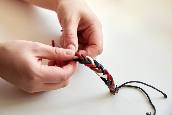 Woman's hands making a leather bracelet on a white background, close-up.