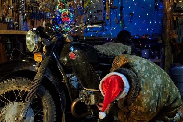 Mężczyzna Kapeluszu Świętego Mikołaja Naprawia Stary Motocykl Garażu Sylwestra — Zdjęcie stockowe