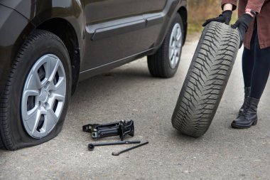 Genç bir kadın arabasının yanında lastiği patlamış, yolda sorun var..