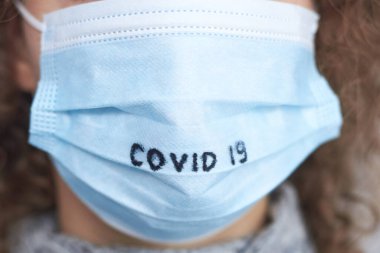 Coronavirus 'a karşı korunma teması olan Covid 19 yazılı tıbbi maske takan bir kadın..