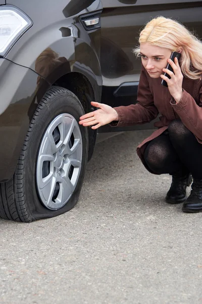 一位金发碧眼的年轻女子在车旁的手机上说着话 车胎漏气 路上遇到了麻烦 — 图库照片