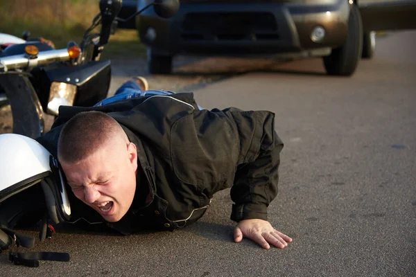 摩托车手躺在摩托车和汽车旁边的沥青路面上 这是交通事故的主题 — 图库照片