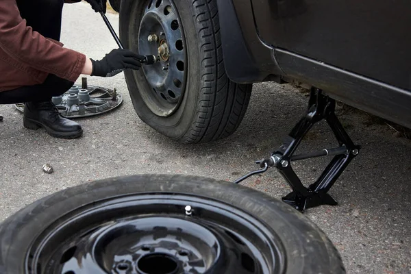 A young woman removes the wheel with a key near her car with a flat tire, trouble on the road.