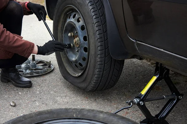 A young woman removes the wheel with a key near her car with a flat tire, trouble on the road.