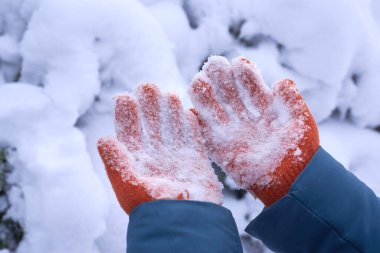 Turuncu eldivenli kadın elleri ve sıkışmış kar, kış zamanı.