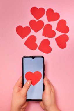 Akıllı telefondan uçan kağıt kalpler, üst görüş, bir kadının elinde Sevgililer Günü, aşk ve teknoloji konsepti..