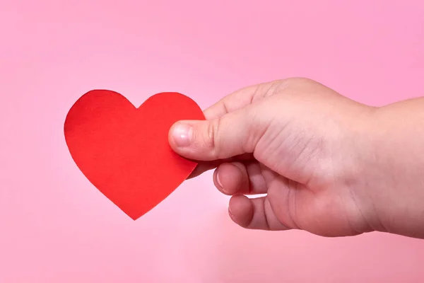 Mano Bambino Tiene Cuore Carta Rossa Uno Sfondo Rosa Tema — Foto Stock