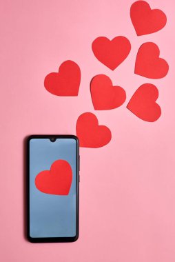 Akıllı telefondan fırlayan kağıt kalpler, üst görünüm, Sevgililer Günü, aşk ve teknoloji konsepti.