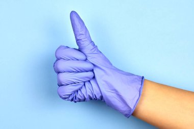 Tıbbi eldiven giymiş bir kadın mavi arka planda bir jest dersi gösteriyor..