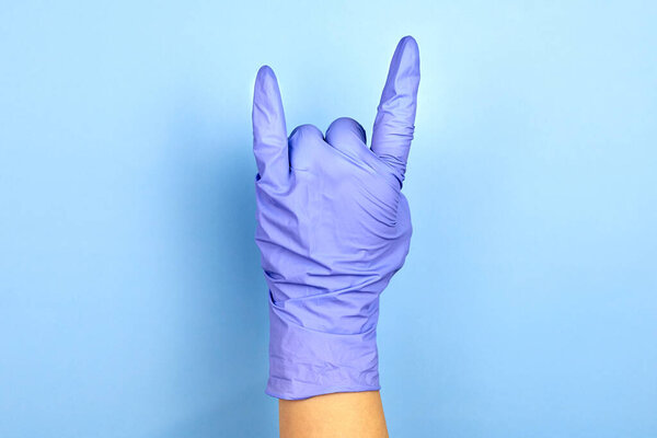 Female hand in medical gloves shows a rock gesture on a blue background.