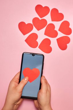 Akıllı telefondan uçan kağıt kalpler, üst görüş, bir kadının elinde Sevgililer Günü, aşk ve teknoloji konsepti..