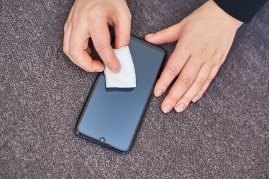 Kadın cep telefonunun ekranını evde alkol peçetesiyle siliyor..