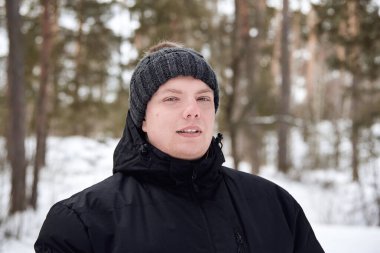 Kış ormanında şapkalı ve ceketli bir gencin portresi..