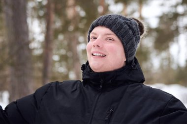 Kış ormanında şapkalı ve ceketli bir gencin portresi..